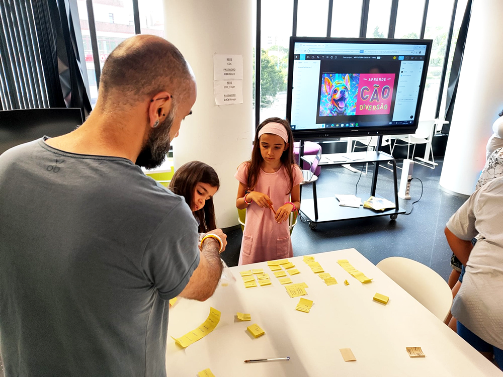 Image of an adult (myself, Pedro Rodrigues) worshopping with 2 children, post-its on a table and tv on the background. This is an image related to a project inside Pedro Rodrigues (Treze413) graphic design portfolio.